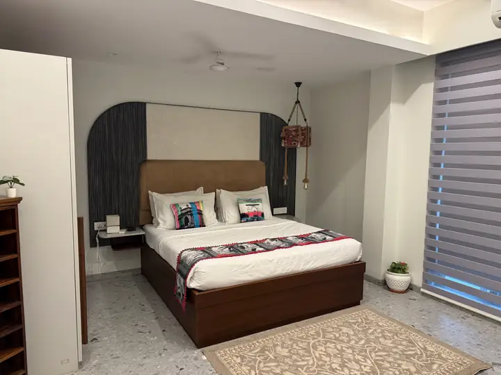 Kamar tidur dengan kasur besar, sandaran kepala kayu, lantai teraso, dan tirai jendela