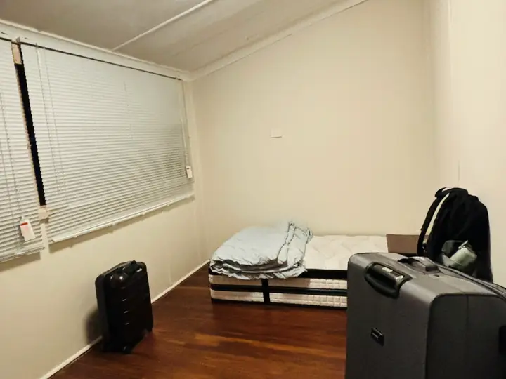 Kamar sederhana berlantai kayu dengan kasur, tirai lipat, dan dinding krem